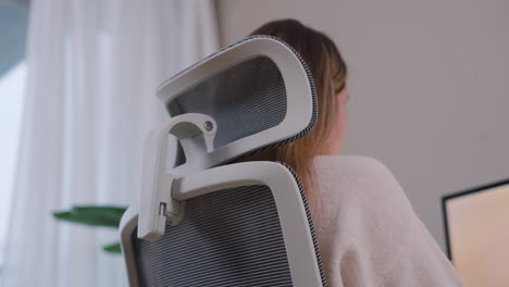 vista lateral trasera de una mujer sentada en una silla de oficina trabajando desde casa