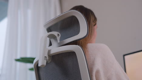 rear side view of a woman seated in an office chair working from home