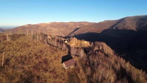 Toma-Aérea-De-Paralaje-Con-Drones-De-Una-Cabaña-De-Madera-Rodeada-De-árboles-Escasos-En-Un-Soleado-Día-De-Otoño,-Cielo-Despejado,-En-La-Zona-De-Apuseni,-Rumania