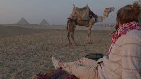 man relaxes in the desert at sunset, pyramids in distance