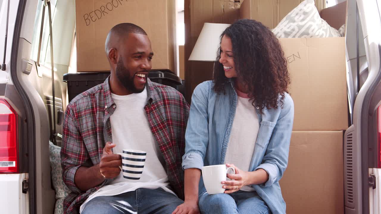 pareja tomando un descanso en la parte trasera del camión de mudanzas el día de la mudanza