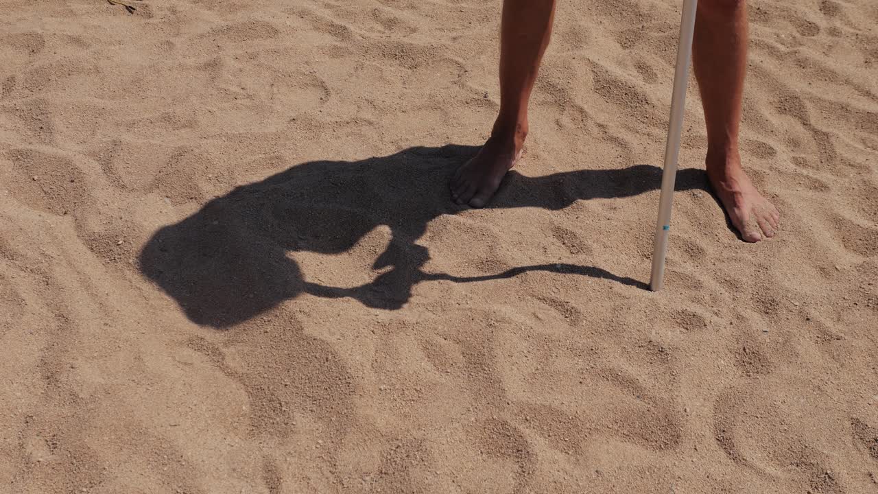 Person's shadow and measuring stick on the beach