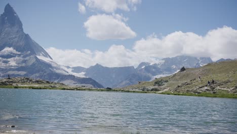 Travelers-walking-along-surrounding-mountainside-landscape-near-large-lake-at-bottom-of-the-Matterhorn-in-Switzerland