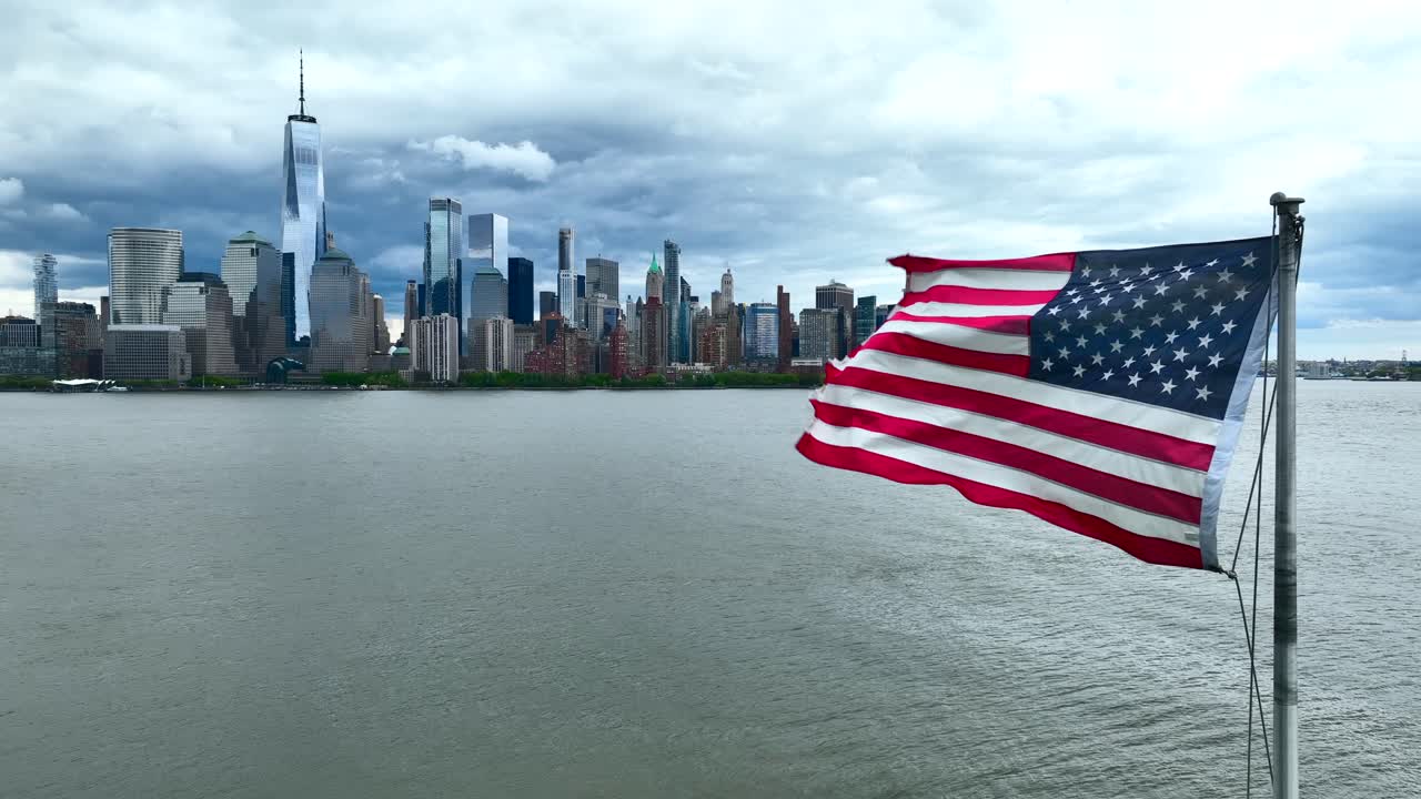 Bandiera americana che sventola con orgoglio con il fiume Hudson e i grattacieli dello skyline di Lower Manhattan a NYC in una giornata estiva nuvolosa e coperta