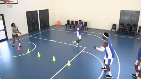 multiracial male basketball players avoiding cones and throwing basketball with coach in gym