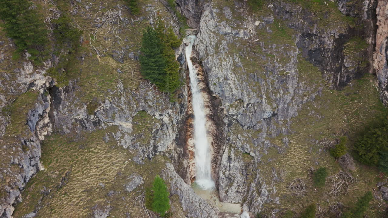 vista aérea de una cascada vertical que cae por acantilados rocosos en los dolomitas, rodeada de terreno alpino