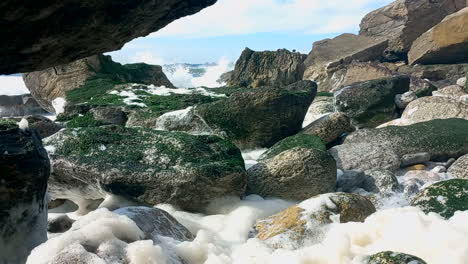 Weißer-Schaum-In-Der-Mitte-Der-Felsen-Mit-Den-Meereswellen,-Die-Auf-Die-Felsen-Mit-Grünem-Moos-Treffen