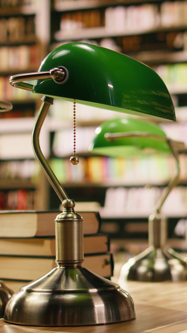 Vertical Video Close up view of stack of books near green lamps on wooden library table