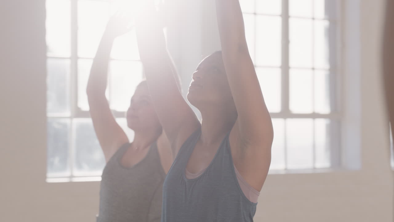 전사 포즈를 연습하는 요가 수업을 듣는 젊은 임신 혼혈 여성은 일출 때 피트니스 스튜디오에서 운동하는 건강한 라이프스타일 그룹을 즐기고 있습니다.