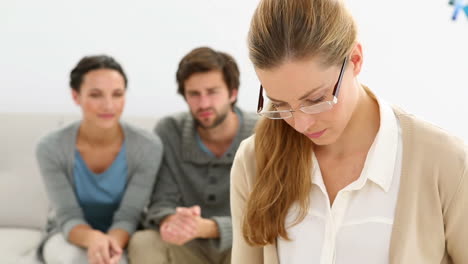 young unhappy couple sitting on sofa behind therapist