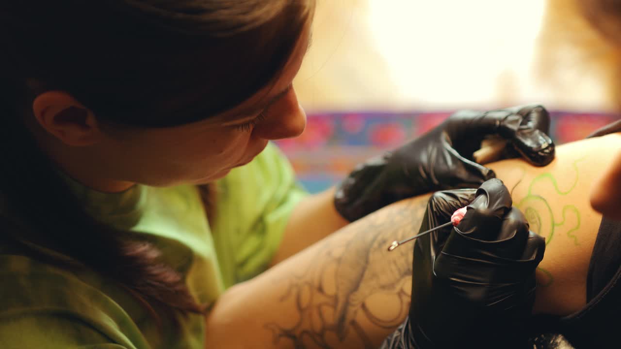 Female Tattooist in Gloves Doing Tattoo on Upper Arm of Woman