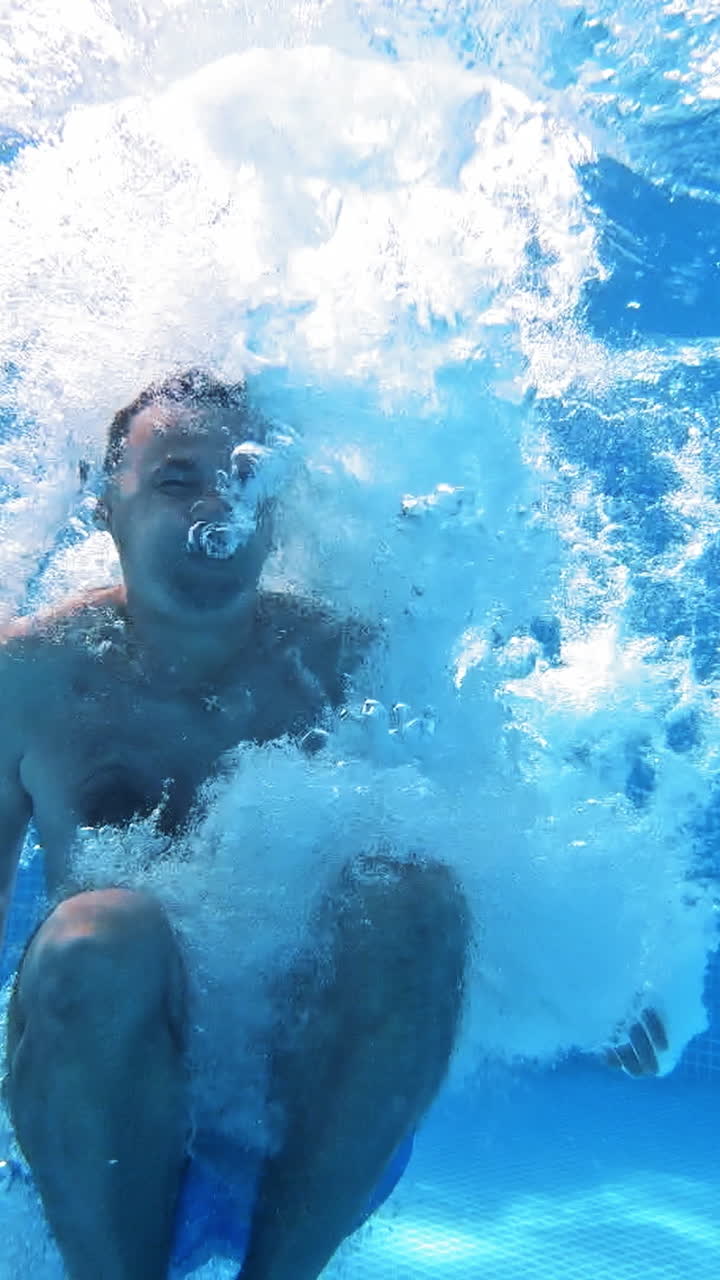 Underwater view of man jumping in the pool, slow motion Vertical video
