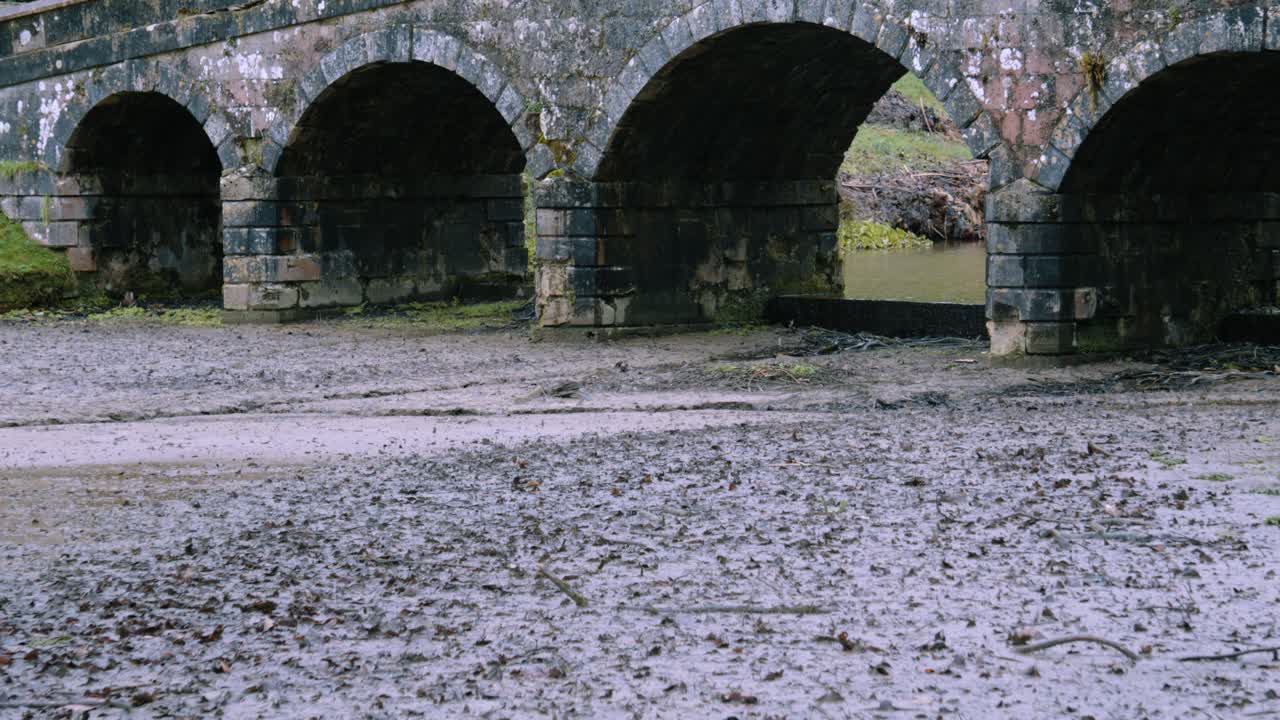 Fango da un lago in ritirata con un vecchio ponte di pietra storico in rovina nel Regno Unito