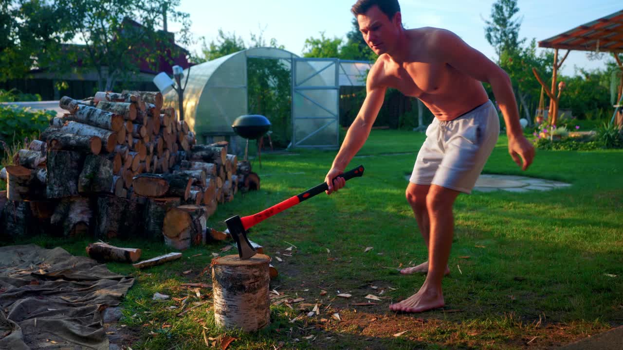 반 벌거벗은 남자가 뒷마당에서 도끼를 사용하여 나무 통나무를 쪼개었다