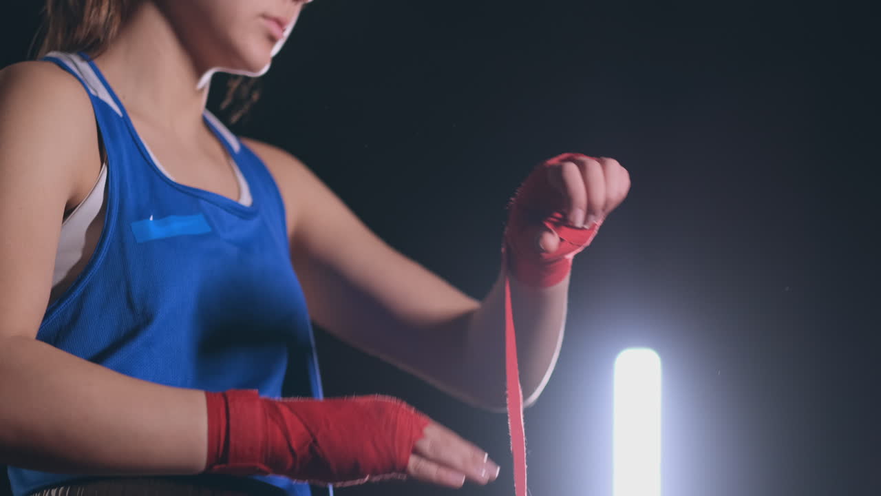 mujer está envolviendo las manos con envolturas de boxeo amarillas. autodefensa para mujeres. aislada en negro con uñas rojas. mano y puño fuertes, lista para luchar y ejercicio activo. steadicam filmado