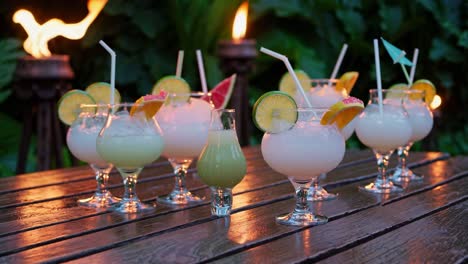 arranging tropical cocktails garnished with fresh fruit slices on a wooden table, illuminated by warm candlelight, creates a relaxing atmosphere in a tropical setting