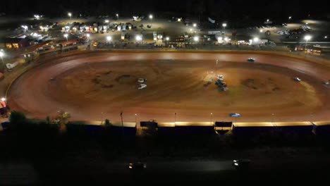 slow aerial flyaway shot of oval dirt track racing at night