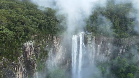 vista cinematográfica volando a través de nubes de niebla para revelar una majestuosa cascada que fluye hacia una selva tropical debajo