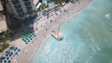 Las-Arenas-Blancas-Se-Encuentran-Con-Una-Gama-De-Sombrillas-De-Playa-En-Esta-Vista-Aérea,-Donde-La-Gente-Disfruta-De-La-Belleza-De-Un-Mar-Tranquilo-Y-Claro.