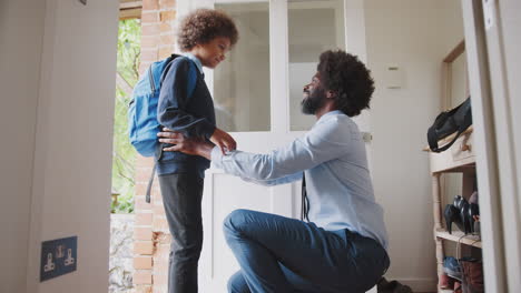 Un-Hombre-Negro-De-Mediana-Edad-Con-Camisa-Y-Corbata-Arrodillado-Preparando-A-Su-Hijo-Y-Despidiéndose-Antes-De-Salir-De-Casa-Para-Ir-A-La-Escuela-Por-La-Mañana,-Vista-Lateral