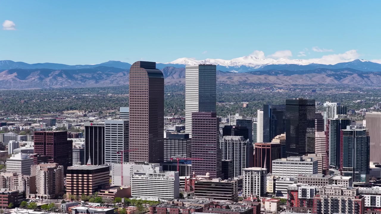 Ripresa aerea con drone di imponenti grattacieli del centro di Denver, circondati dalla griglia urbana e con montagne all'orizzonte.