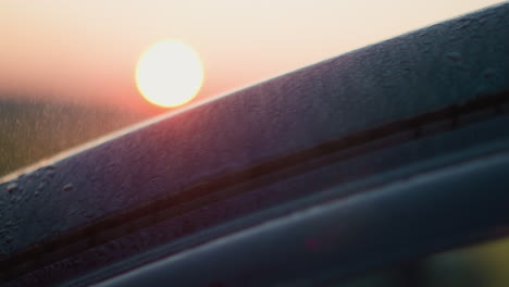 rain falls on car against dusk sun closeup wet auto surface stands under rainstorm in evening