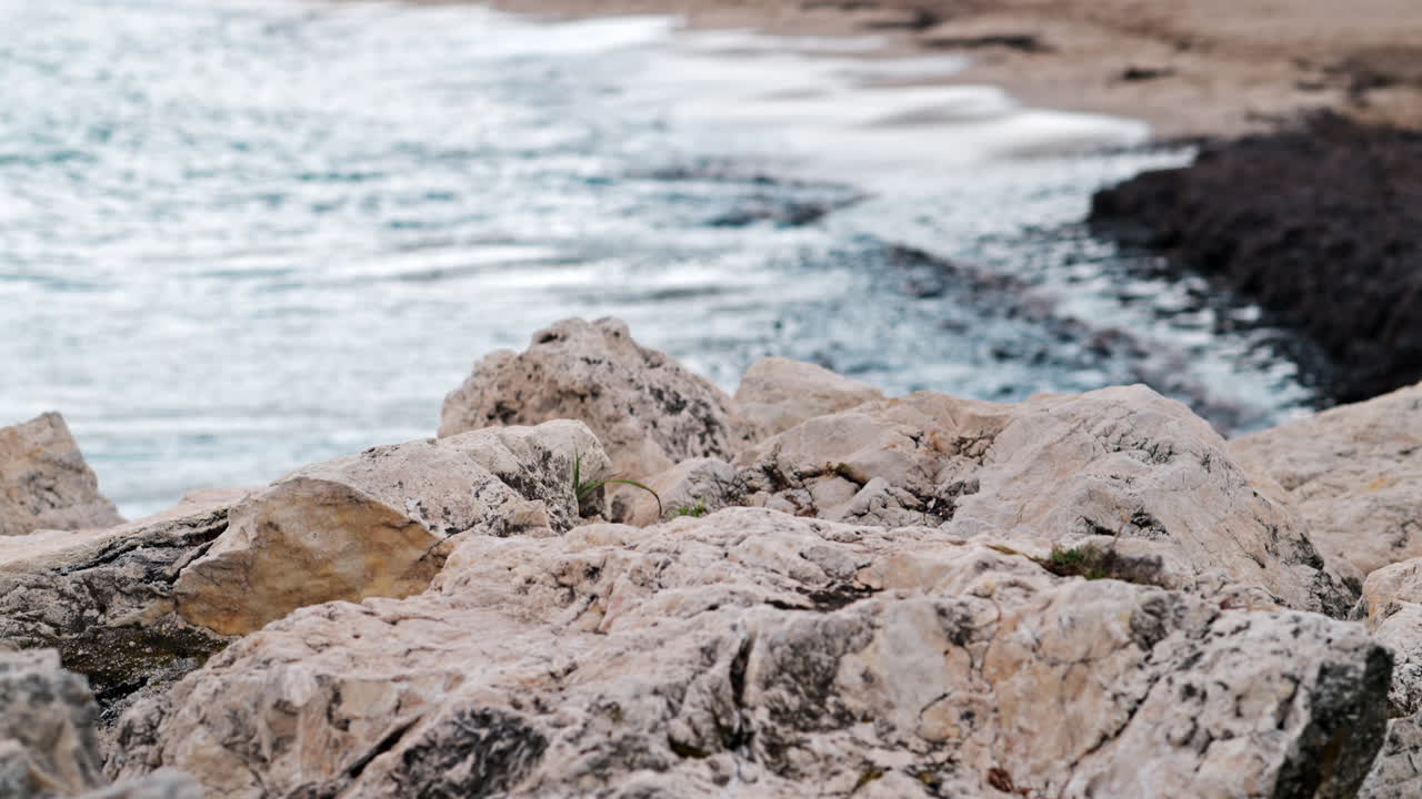 Primo piano di rocce bianche e frastagliate con onde scure che si infrangono su una riva fangosa sullo sfondo