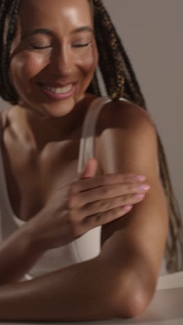 studio skincare beauty shot of woman dispensing moisturiser and pretending to rub it into camera lens 1