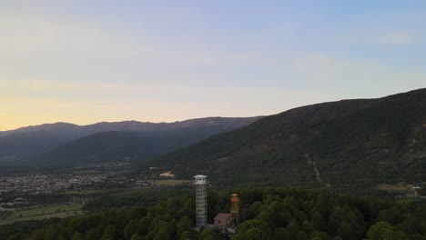 reverse flight with dro visualizing a fire surveillance post located at the top of a hill and a town, with mountains in the background