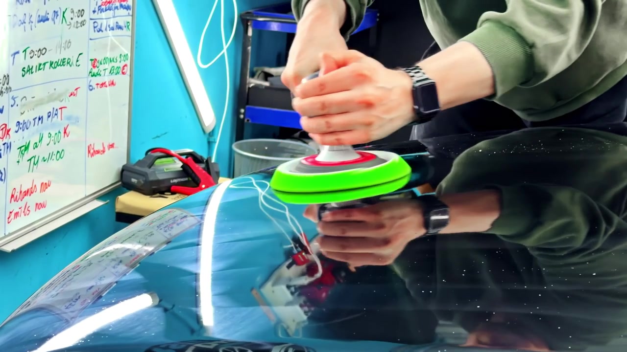 Person polishing car hood with electric buffer in workshop, close-up action shot
