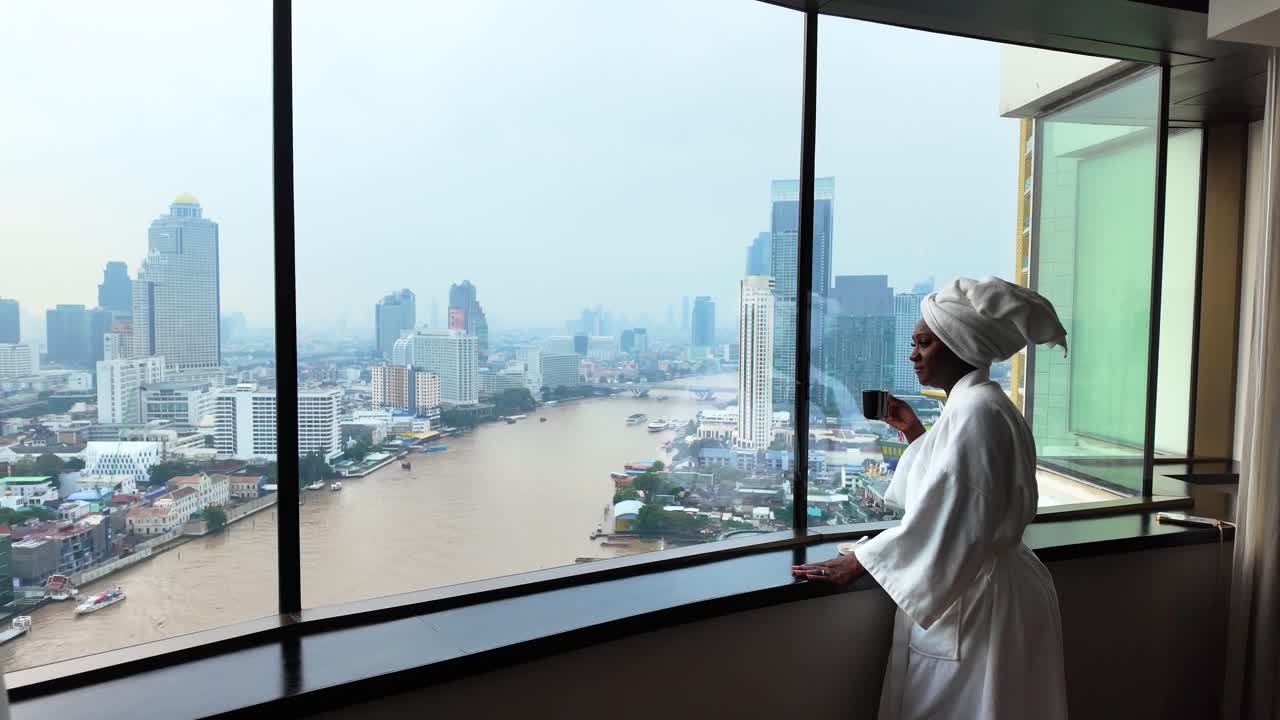 Donna africana che si rilassa vicino alla finestra di Bangkok, vista urbana, atmosfera serena mattutina