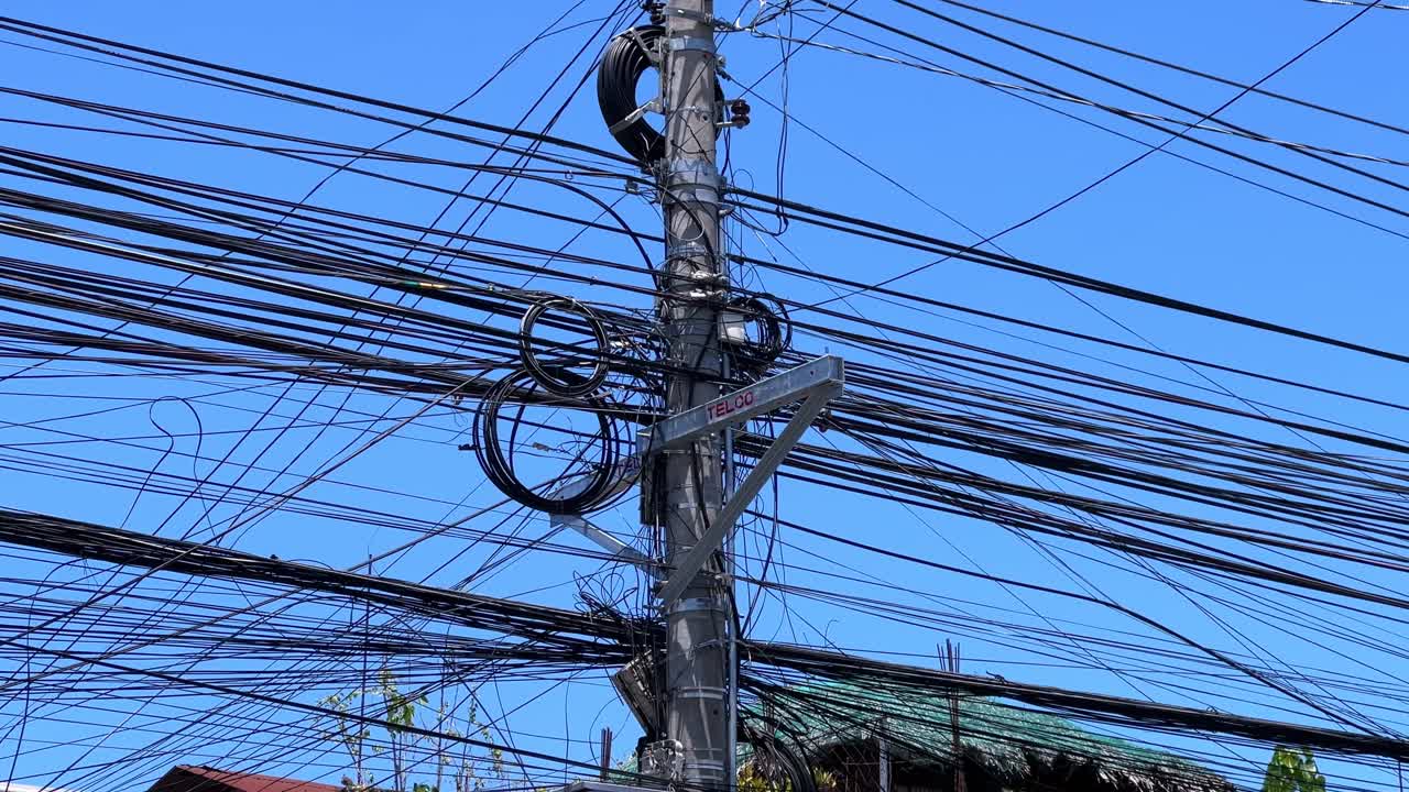 Dense web of tangled power and telecom cables on a utility pole under clear blue sky. Perfect for editorial, infrastructure, and urban decay themes