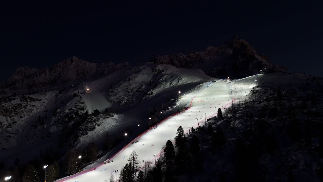 Drone shot of Cortina ski slopes at night in the Dolomites with illuminated Olympic scenery