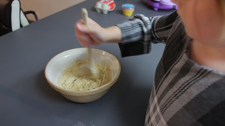 A girl mixing cookie dough cake mixture in a bowl with a wooden spoon