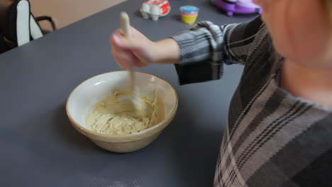 a girl mixing cookie dough cake mixture in a bowl with a wooden spoon