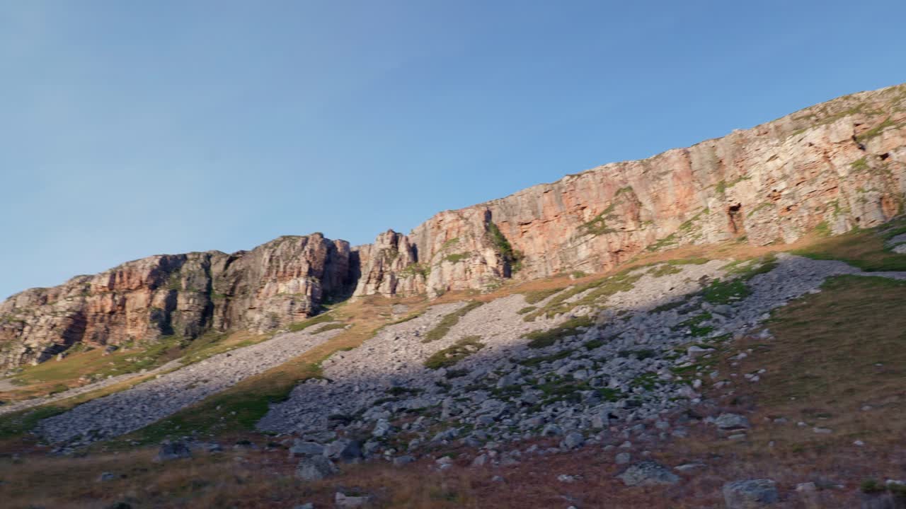 una toma panorámica lenta de un imponente acantilado en las tierras altas del noroeste mientras el sol de la tarde se pone y los rayos de luz alcanzan la cresta