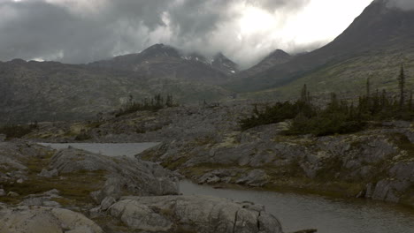 múltiples montañas nubladas se encuentran más allá de un río tranquilo, tomadas desde un tren que se mueve lentamente