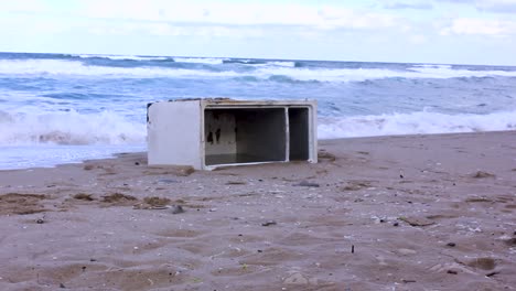 old fridge washed ashore on beach with sea waves crashing in background