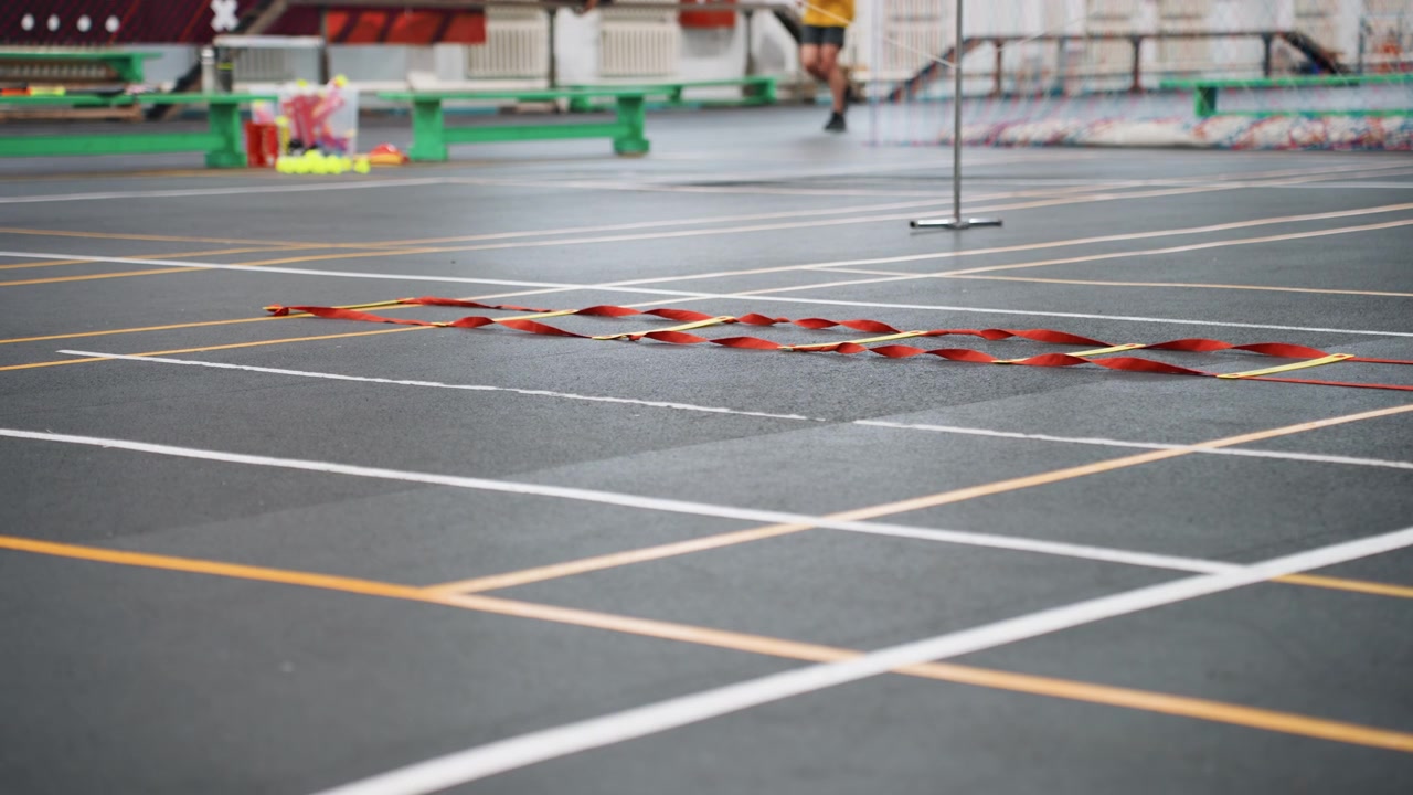 Campo da badminton vuoto con rete e linee del campo chiare su pavimento lucido interno, panchine distanti e attrezzatura verde, pochi spettatori, atmosfera tranquilla pre-allenamento, composizione grandangolare che mostra