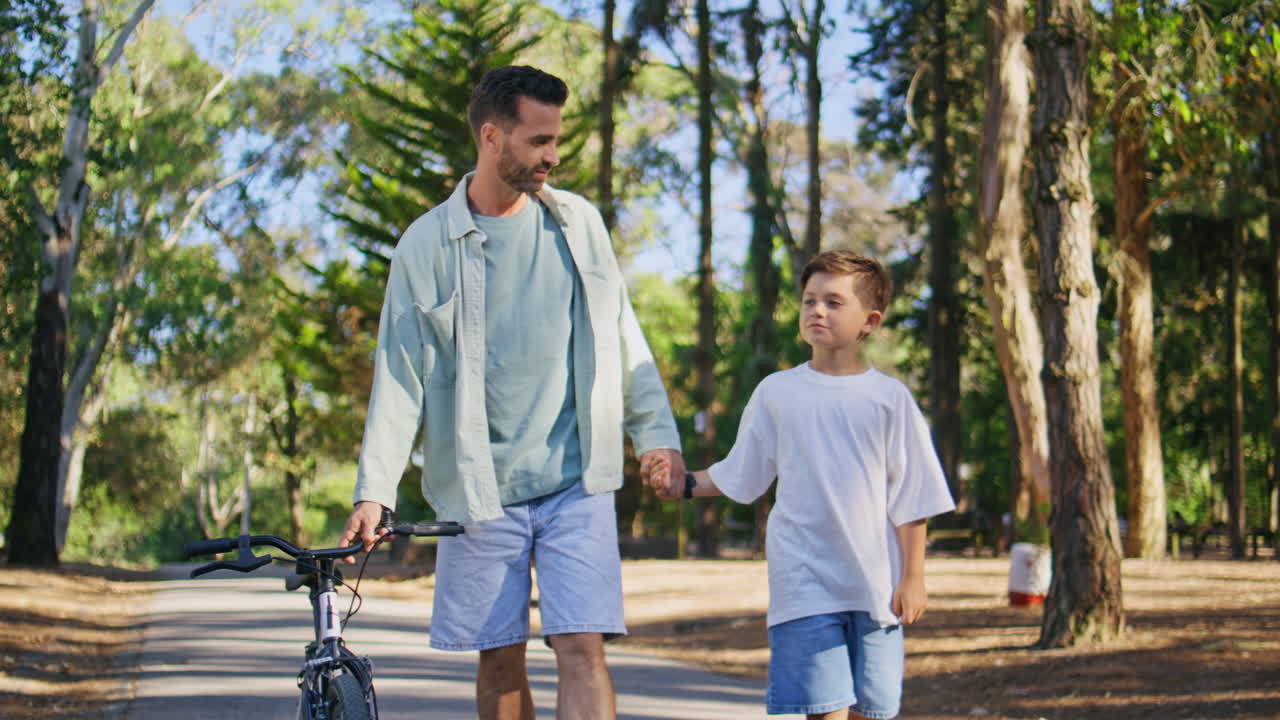 Positive family holding hands talking during walk. Man boy walking sunshine path