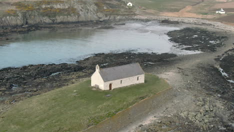 an aerial view of eglwys cwyfan church on an overcast day, flying right to left around the church, anglesey, north wales, uk