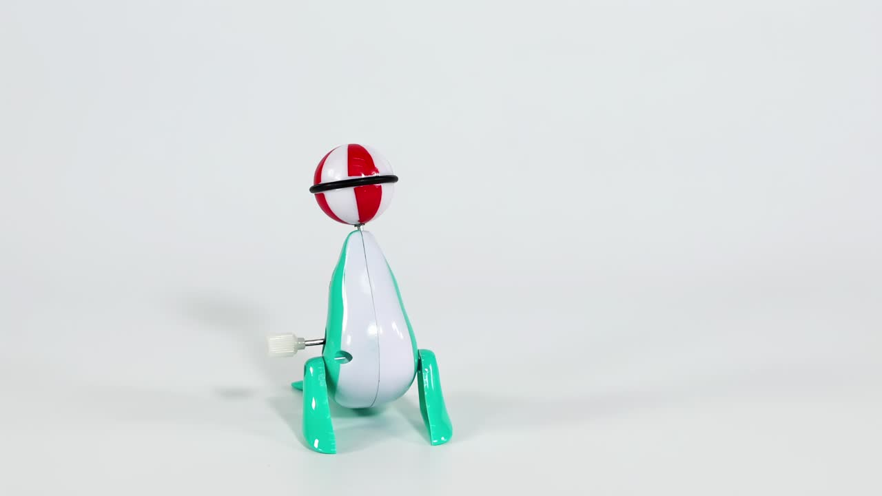 A green toy dinosaur skillfully balances a red and white ball on its nose.