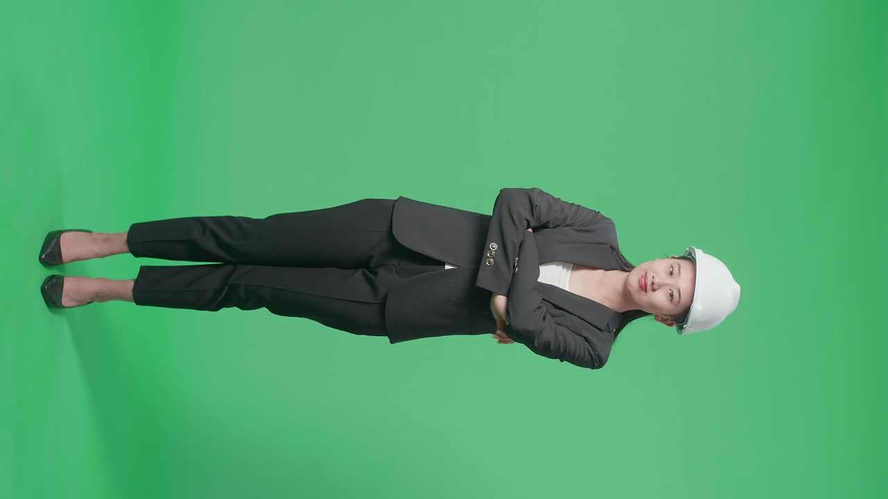 Full Body Of Smiling Asian Female Engineer Putting On The Safety Helmet And Crossing Her Arms In The Green Screen Studio