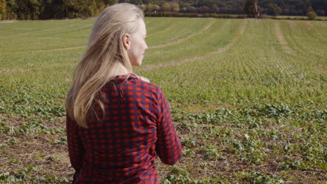 a blonde woman in a plaid shirt stands in a rural field