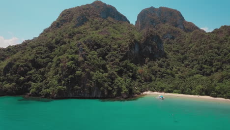 Toma-Aérea-En-Movimiento-Lento-De-Una-Hermosa-Playa-De-Arena-Blanca-Con-Un-Bote-Pequeño-Y-Montañas-A-Su-Lado,-Palawan-Filipinas