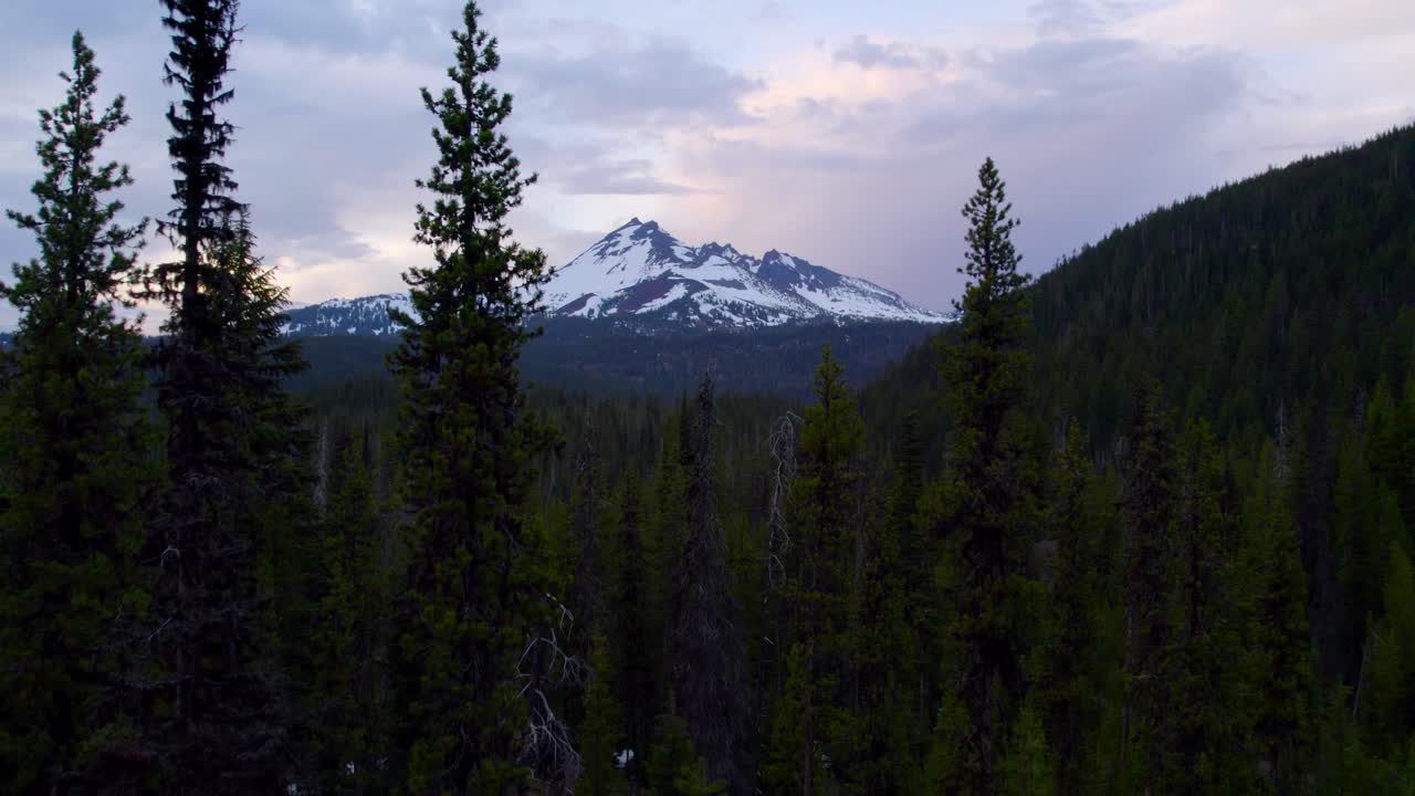 Broken Top mountain at sunset. Drone flying through trees toward snow capped peak. 4K.