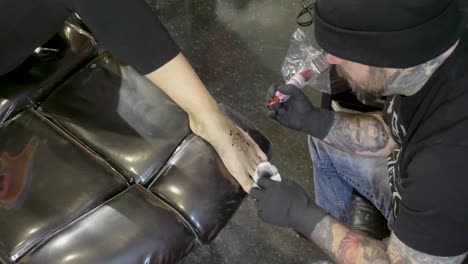 tattoo artist placing small black and white tattoo on ladies foot wide shot