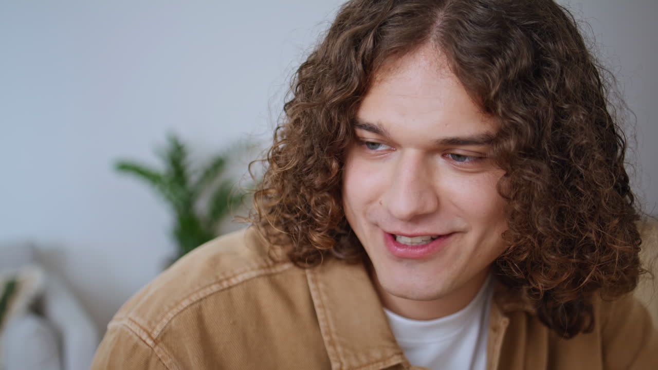 Curly man talking unknown interlocutor in apartment closeup. Portrait trendy guy