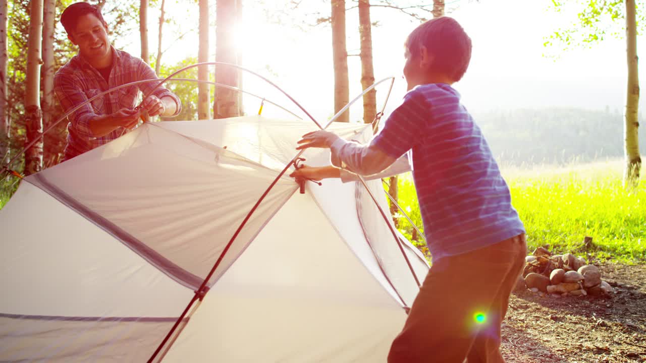 백인 아버지와 아들이 야외에서 텐트를 조립하고 있습니다.
