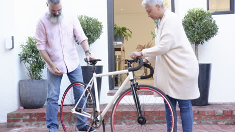 fixing bicycle together, senior couple enjoying outdoor activity in front yard